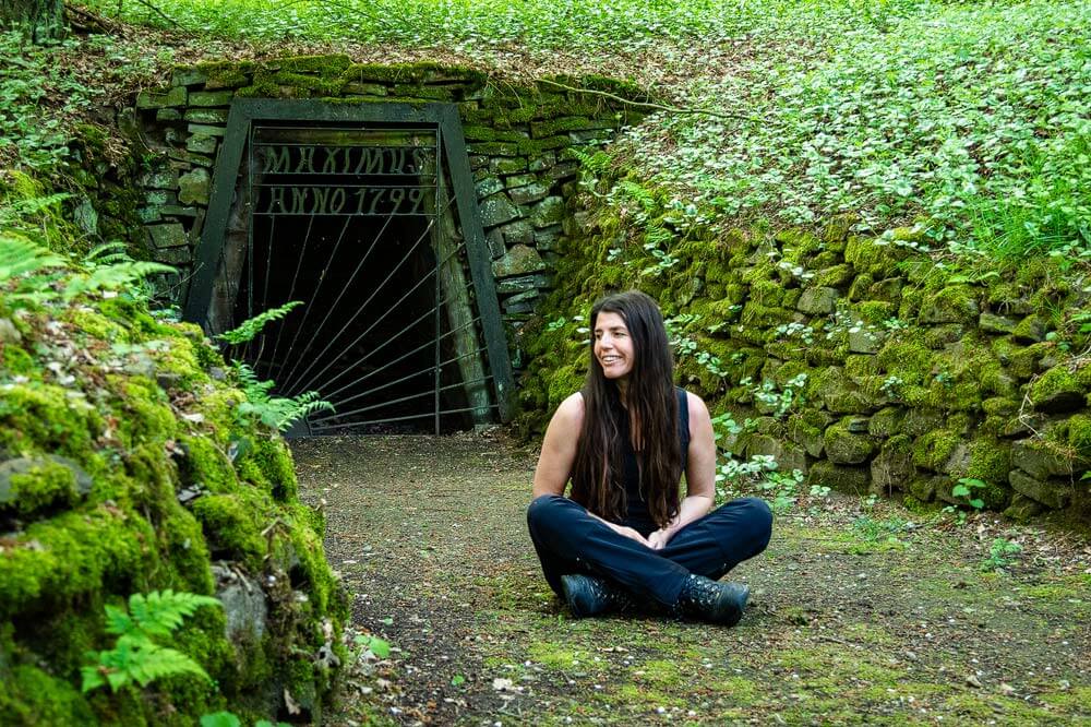 Wanderin macht Pause vor einem alten Stollen auf dem Bergbauwanderweg im Muttental in NRW
